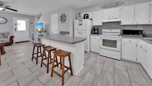 A modern kitchen with white cabinets, a large island with stools, a coffee maker, and a microwave. - Sand Castles West T24 (Panama City Beach)