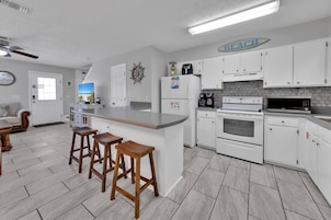 A modern kitchen with white cabinets, a large island with stools, a coffee maker, and a microwave.