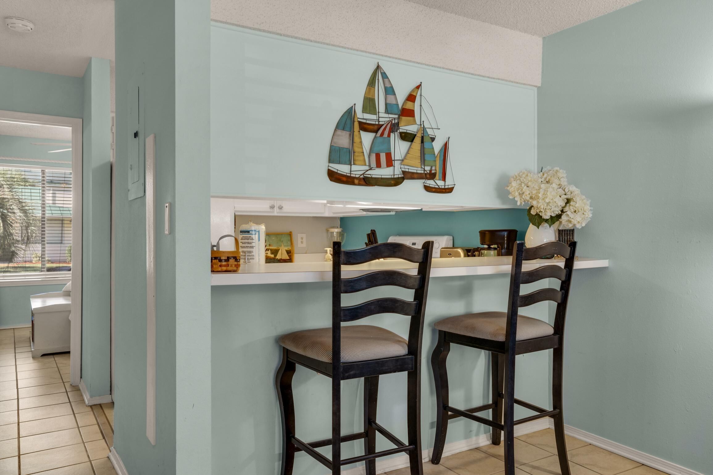 A kitchen with two wooden bar stools, a white countertop, and a wall-mounted sailboat decoration.