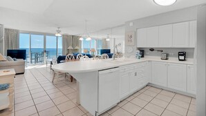 A modern kitchen with white cabinetry, a central island with a sink, and a dining area with chairs. - Island Princess 315 (Fort Walton Beach)