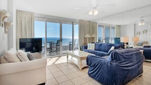 A spacious living room with a large window overlooking the sea, a ceiling fan, and a flat-screen TV. - Island Princess 315 (Fort Walton Beach)