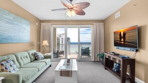 A spacious living room with a green sofa, a coffee table, a TV, and a balcony with a view of the ocean. - Ariel Dunes I 1404 (Miramar Beach)