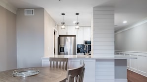 Une cuisine moderne avec des meubles blancs, des appareils en acier inoxydable et des luminaires suspendus.