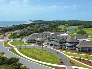A residential area with houses, a curved road, and a body of water in the background. - Gorgeous Sunsets on Pelican Beach! Walk to Pools! Amenity Access included! 2 Dogs - 30# max (Seabrook Island)