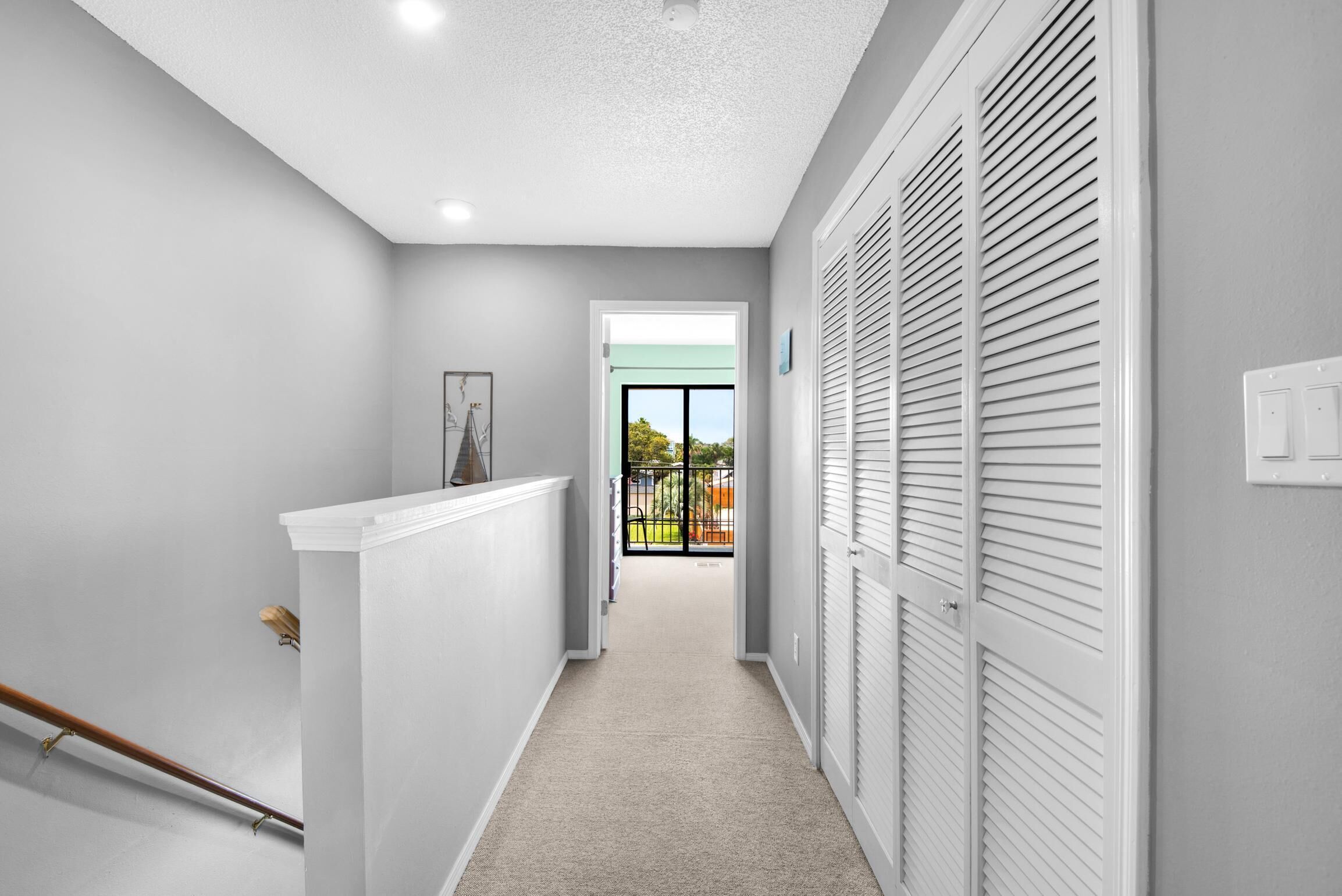A hallway with a white ceiling, grey walls, and a carpeted floor. There is a white door on the right and a window on the left.
