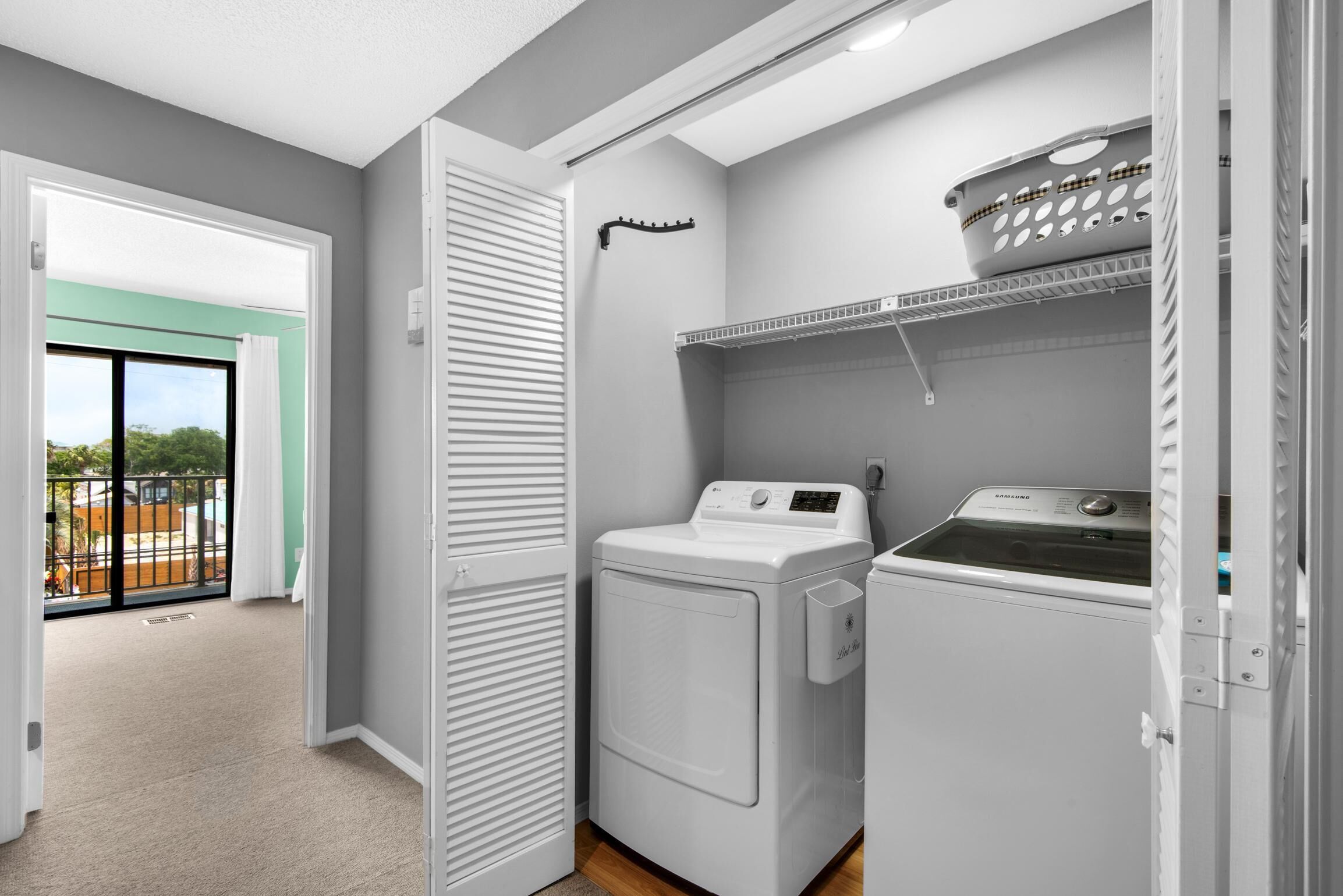 A laundry area with a washing machine and dryer, a drying rack, and a door leading to a balcony.