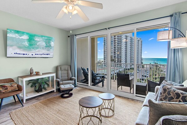 A modern living room with a large sliding glass door leading to a balcony with a view of high-rise buildings and the ocean. - Ariel Dunes I 606 (Miramar Beach)
