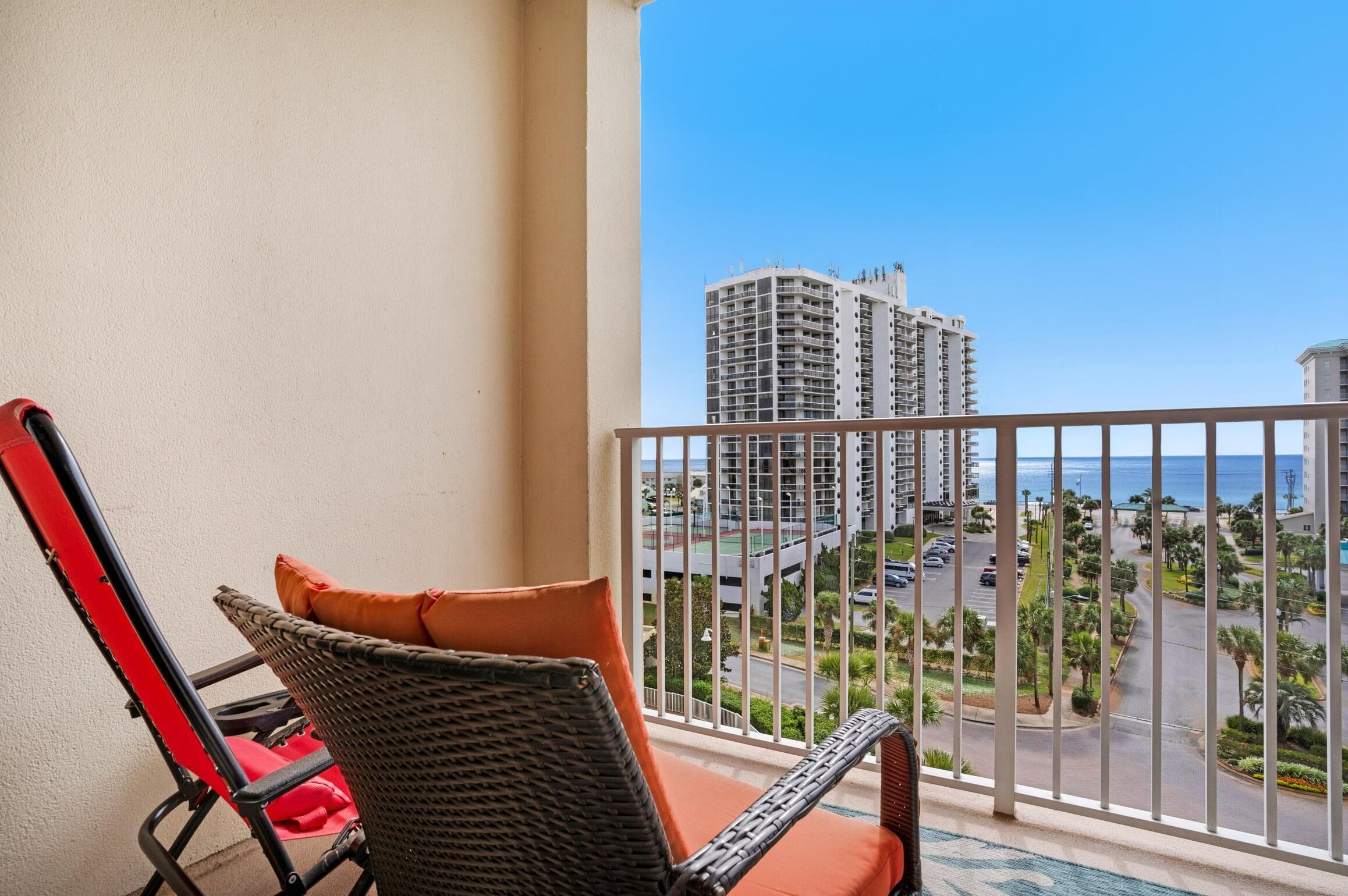 A balcony with wicker chairs and a view of a cityscape and ocean.
