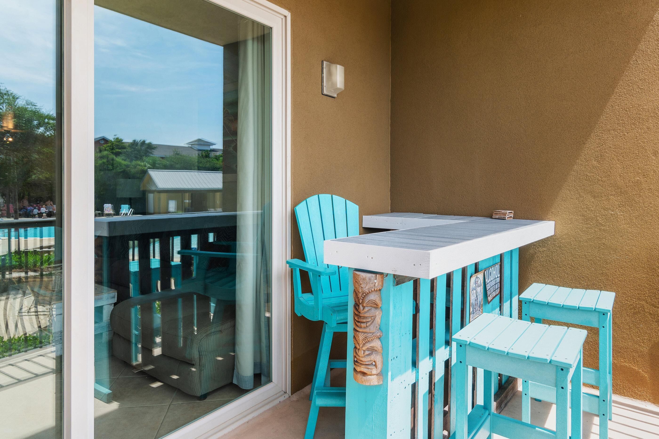 A balcony with turquoise chairs and a table, glass doors, and a view of the outside.