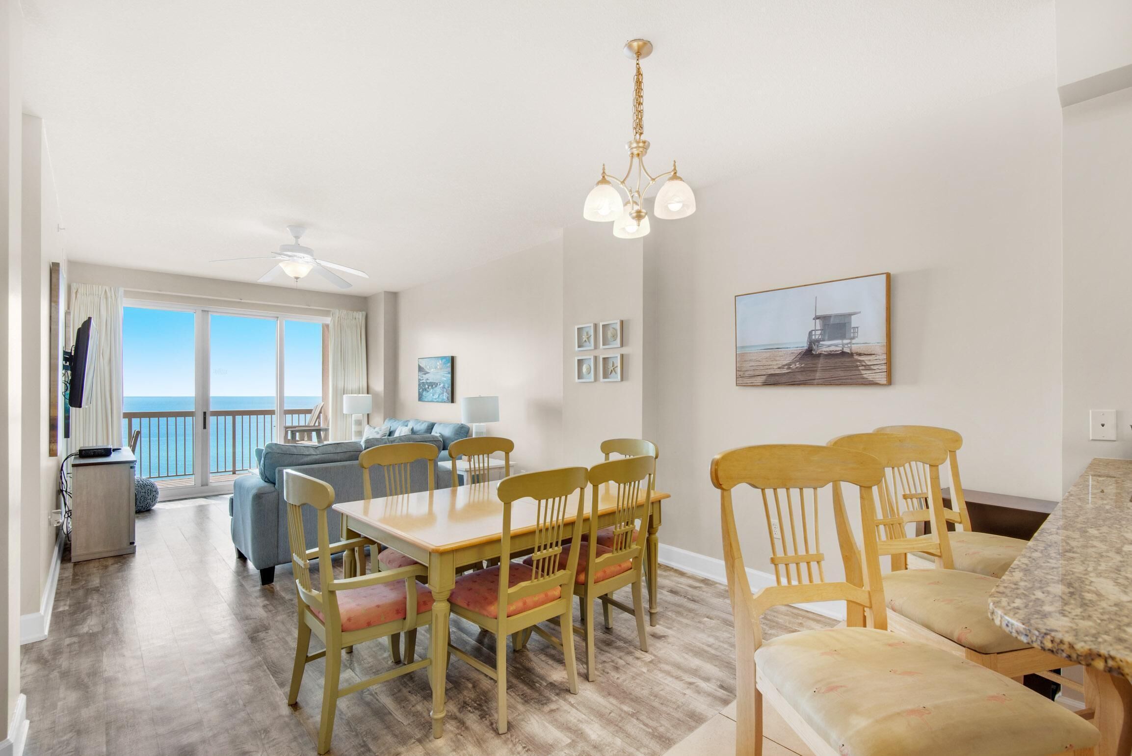 A spacious living area with a dining table and chairs, a balcony with a view, and a ceiling fan.