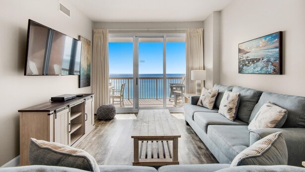 Een moderne woonkamer met een bank, een salontafel en een televisie. Er is een balkon met uitzicht op zee.