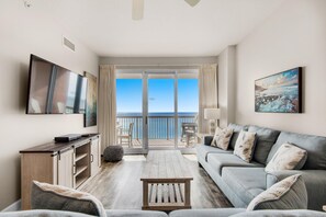 Een moderne woonkamer met een bank, een salontafel en een televisie. Er is een balkon met uitzicht op zee.