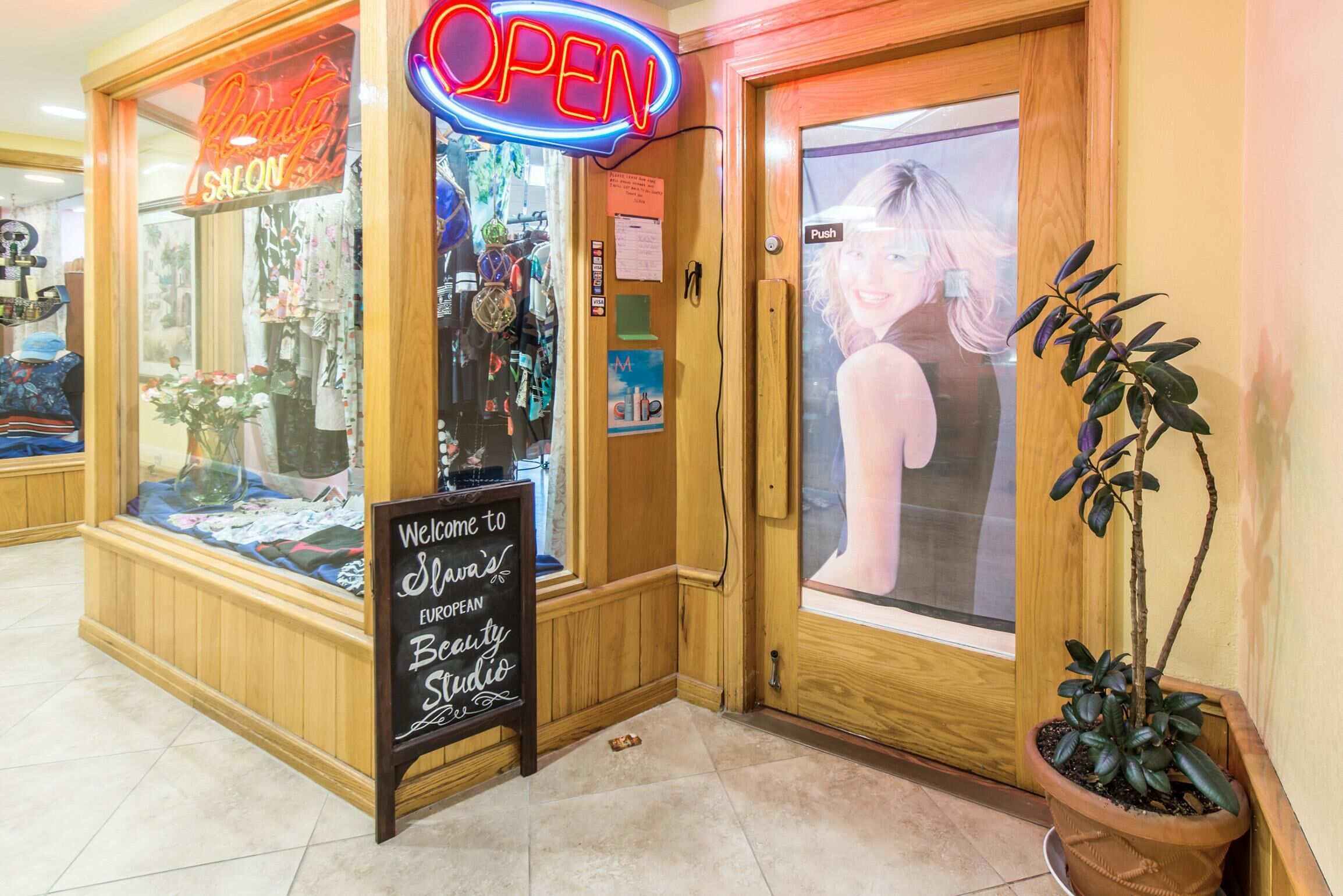 A salon with a neon 'OPEN' sign, a welcome sign, and a potted plant.