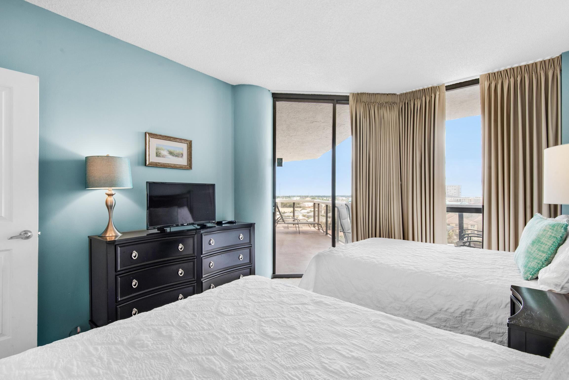 A hotel room with two beds, a TV, a dresser, and a balcony with a view.