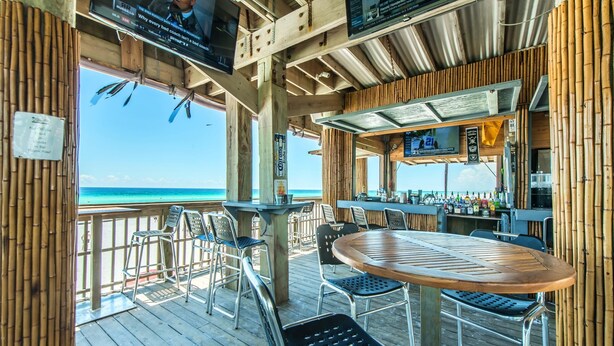 A wooden deck with a round table and chairs, overlooking a beach.
