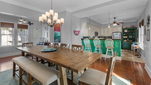 A spacious dining area with a wooden table and benches, a kitchen with white cabinets, and a green island. - Blue Mountain Breeze (Santa Rosa Beach)