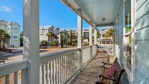 A covered porch with a wooden bench and railing, overlooking a street with houses and palm trees. - Blue Mountain Breeze (Santa Rosa Beach)