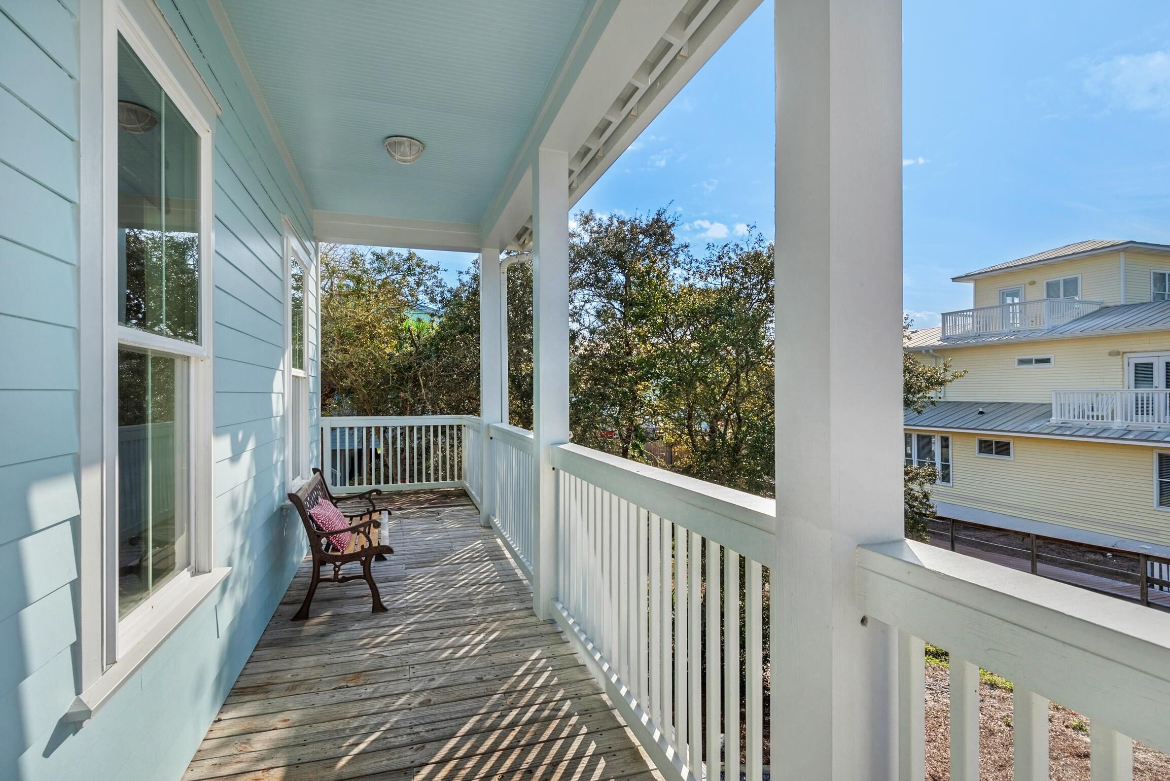 A covered porch with a wooden deck, white railings, and a bench.