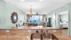 A modern kitchen with granite countertops, a double sink, and a dining area with a view. - Sterling Shores 502 (Destin)