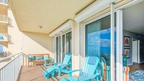 A balcony with blue Adirondack chairs, a wooden bench, and a view of the ocean through large glass doors. - Sterling Shores 502 (Destin)