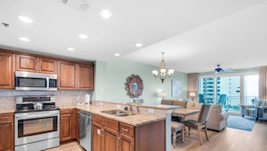 A modern kitchen with wooden cabinets, stainless steel appliances, and a dining area with a chandelier. - Sterling Shores 502 (Destin)