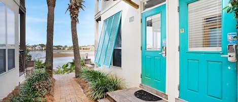A turquoise door with a mailbox, a wooden bench, and a small garden with palm trees and plants.