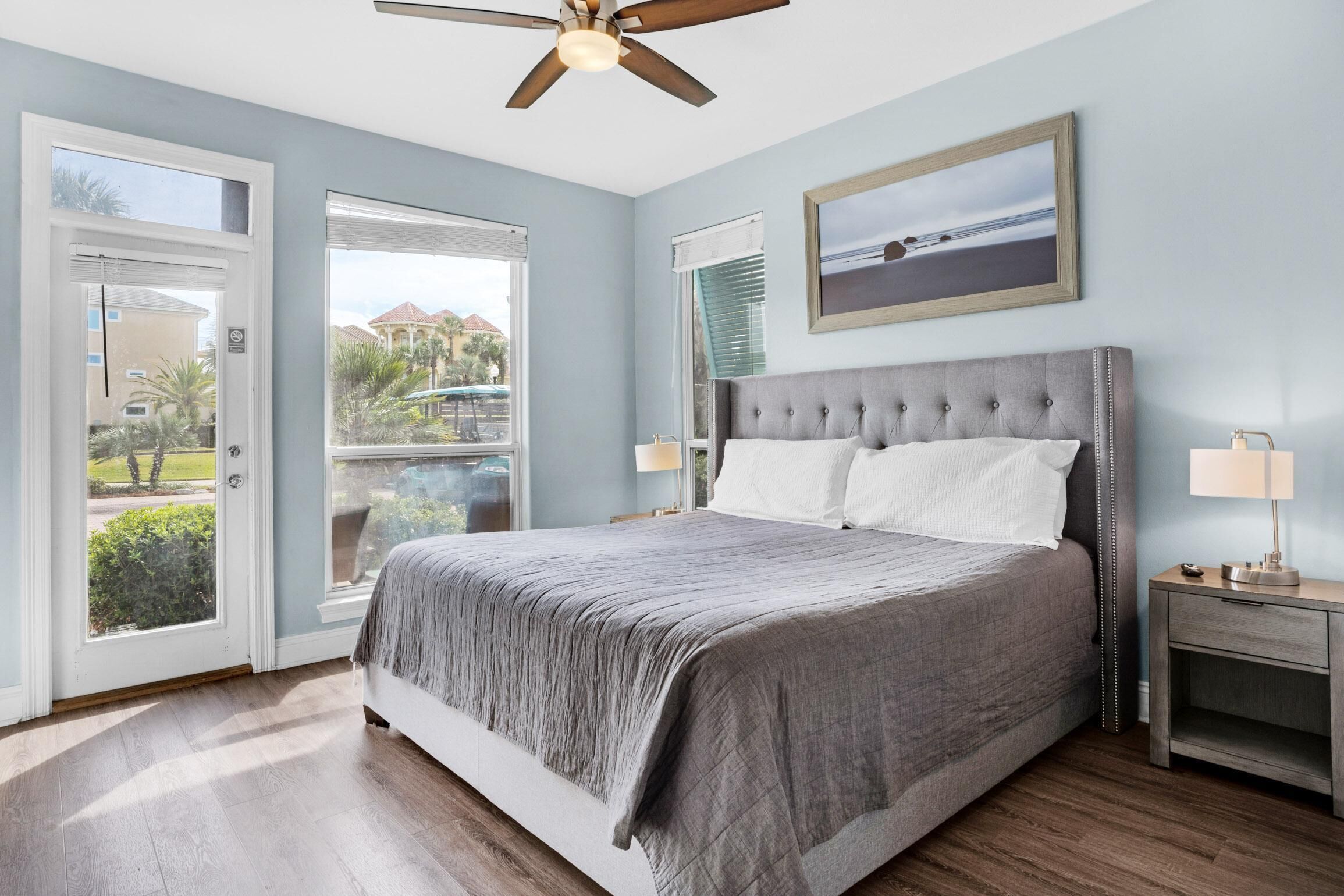 A bedroom with a large bed, a ceiling fan, a nightstand, and a window with a view of the outside.