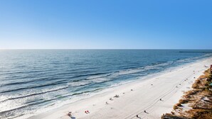 A beach with a pier extending into the ocean, clear skies, and people sunbathing. - Majestic Beach Towers 1-1210 (Panama City Beach)