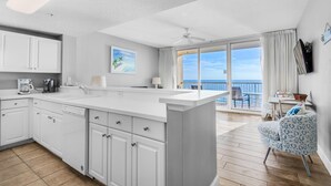 A modern kitchen with a large island, white cabinetry, and a view to a balcony with a chair and table. - Majestic Beach Towers 1-1210 (Panama City Beach)
