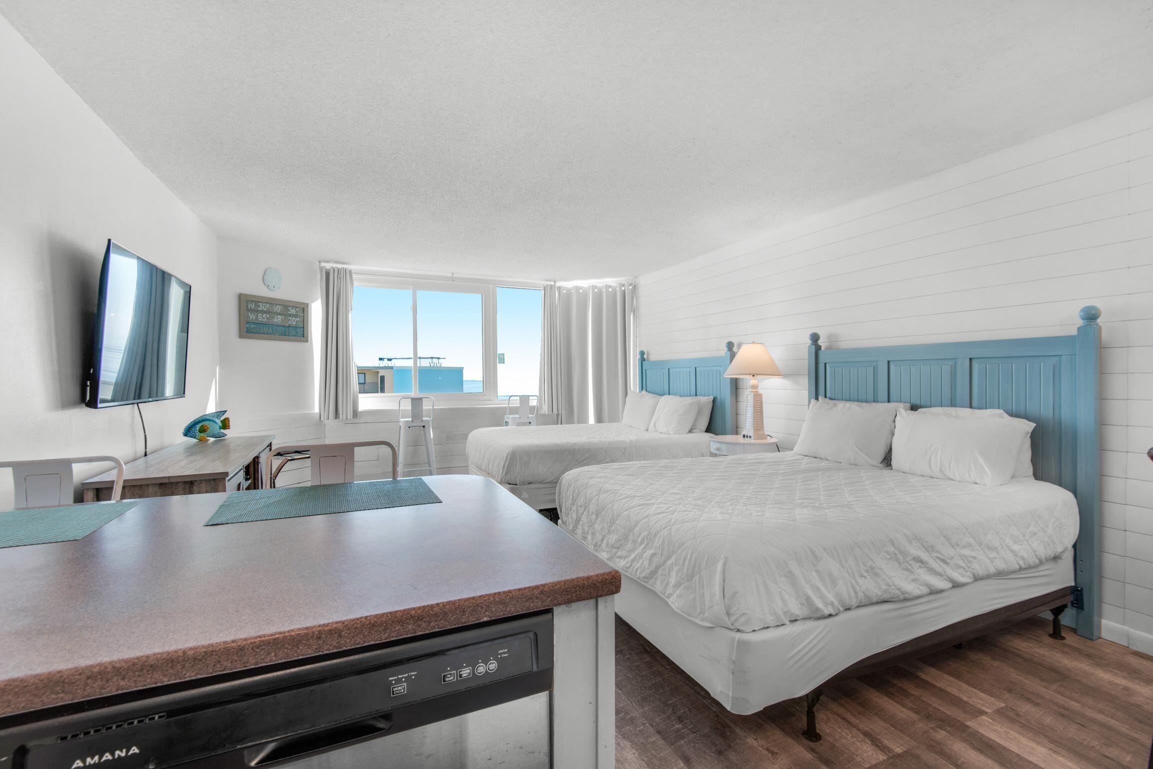 A hotel room with two beds, a desk with a dishwasher, a TV, and a window with curtains.