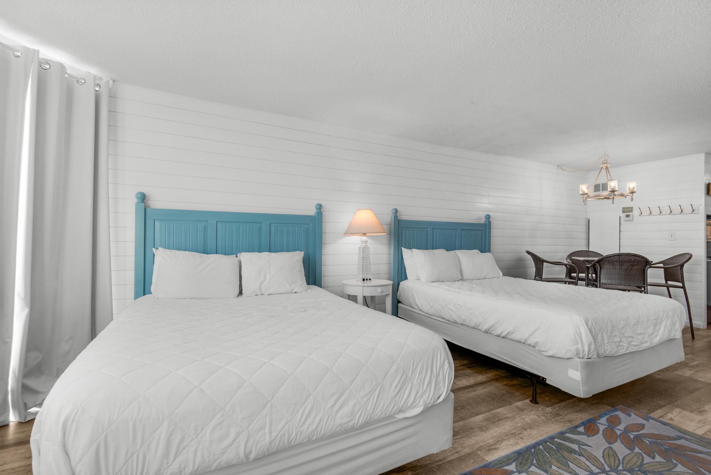 A hotel room with two beds, a small table, a chair, and a chandelier.