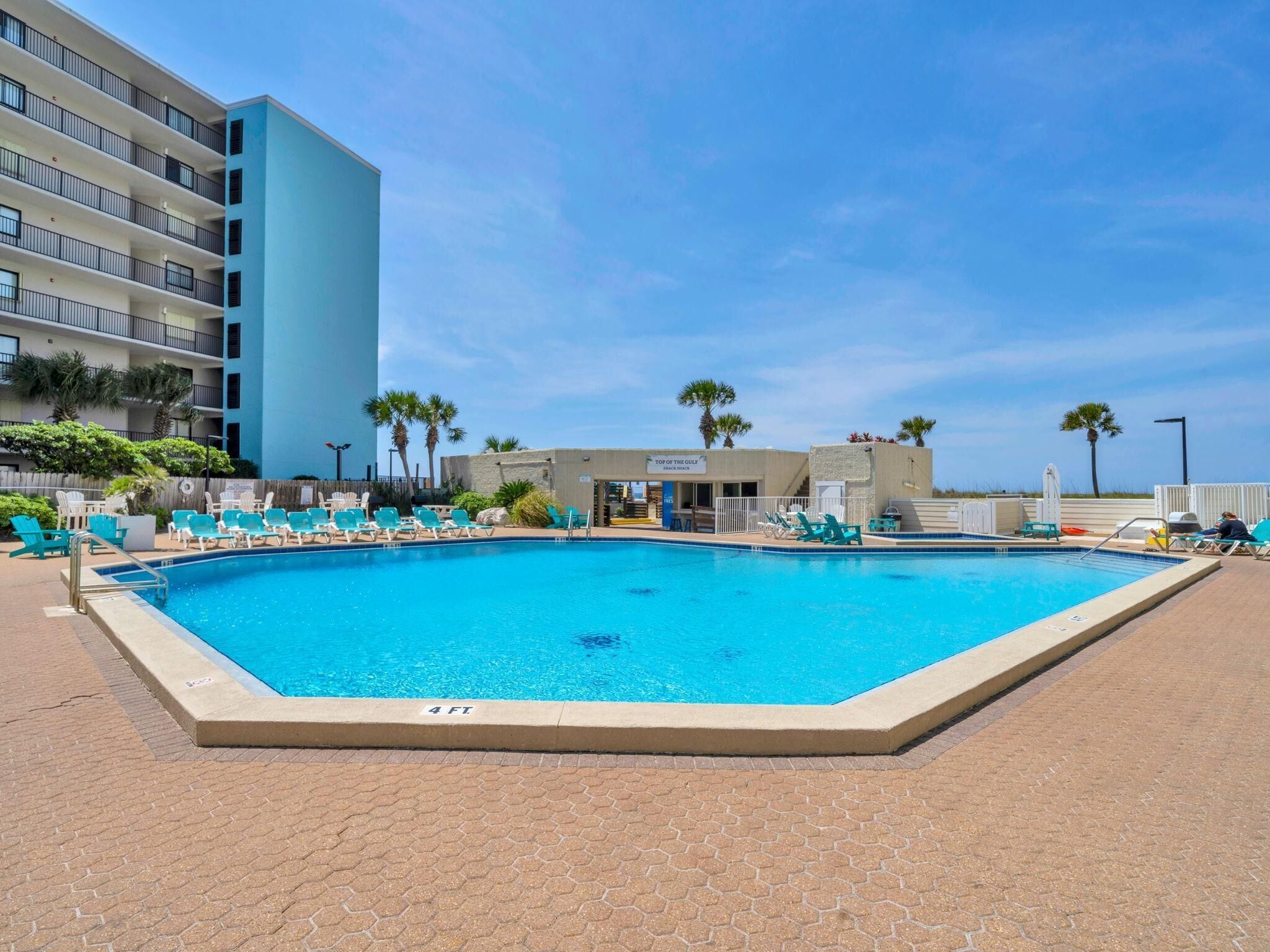 Una piscina con sillones de descanso, un edificio con balcones y palmeras.