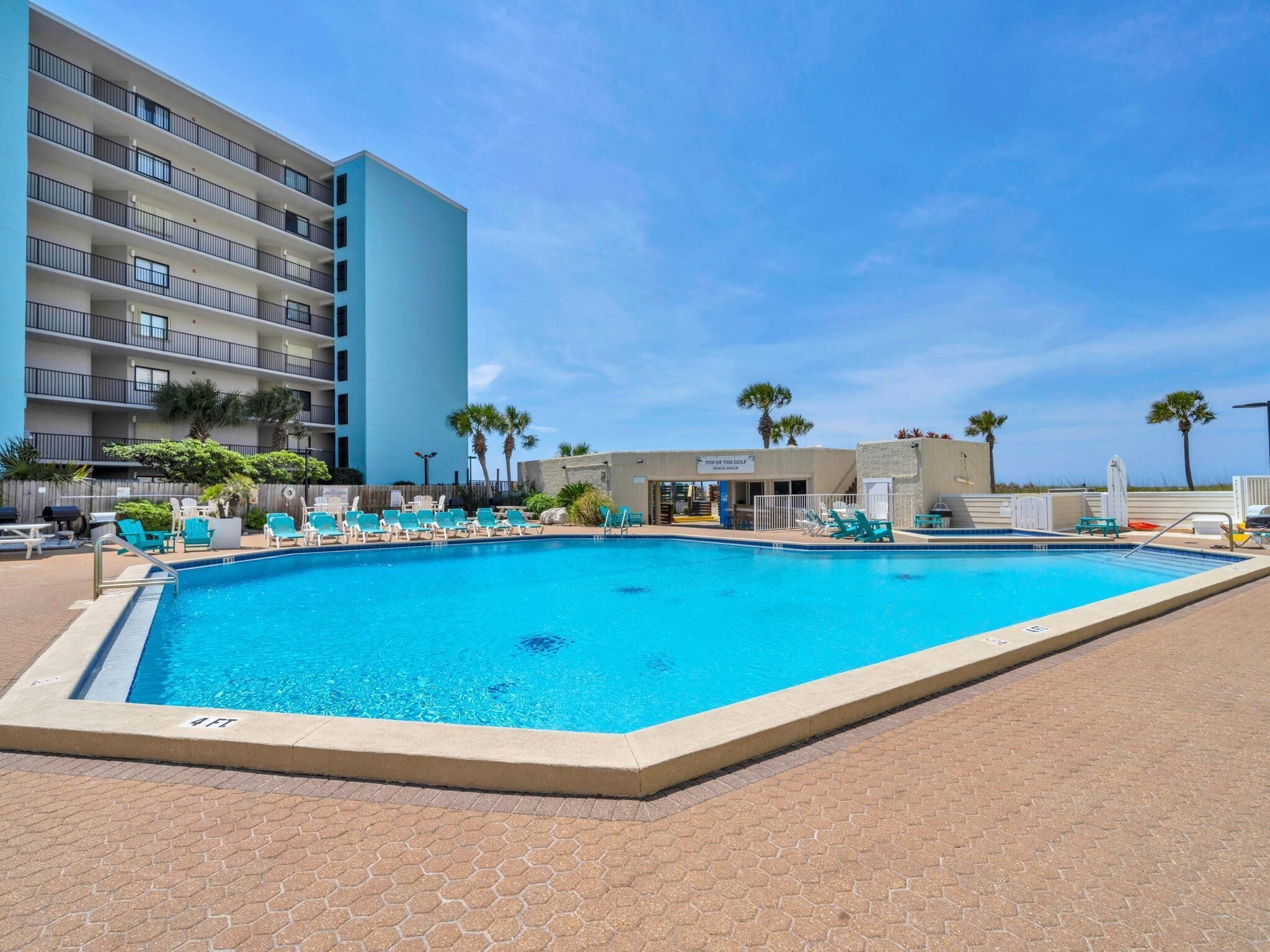 A swimming pool with lounge chairs, a building with balconies, and palm trees.
