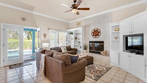 A spacious living room with a ceiling fan, a fireplace, and a television. - Blue Pelican (Destin)