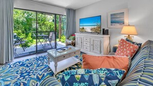 Un salon avec une grande fenêtre, un téléviseur, un canapé et un tapis à motifs.