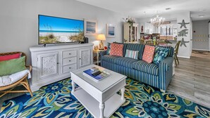 Un salon décoré dans le style balnéaire, avec un tableau sur le thème de la plage, un canapé à rayures, un meuble blanc et un tapis à motifs.