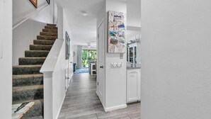 Un escalier menant à un couloir doté d’un plancher en bois, de murs blancs et d’une porte ornée de motifs évoquant la Floride.