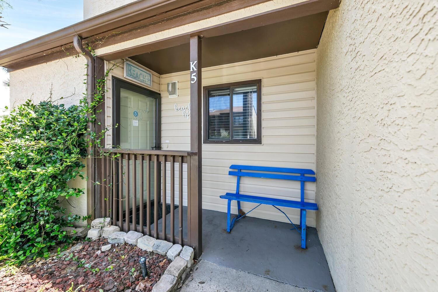 A building entrance with a porch, a bench, and a door marked "Beach."