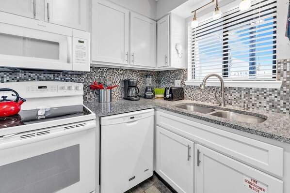 A modern kitchen with white cabinets, a microwave, a stove, and a sink.