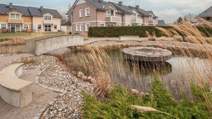 Un quartier résidentiel avec des maisons, un pont et un étang agrémenté d’une structure circulaire en pierre.