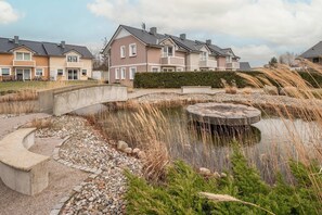 Quartiere residenziale con case, un ponte e uno stagno con un elemento decorativo in pietra circolare.