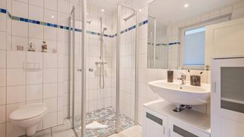 Ein modernes Badezimmer mit einer gläsernen Duschkabine, einem weißen Waschbecken mit Spiegel darüber und einer Toilette.