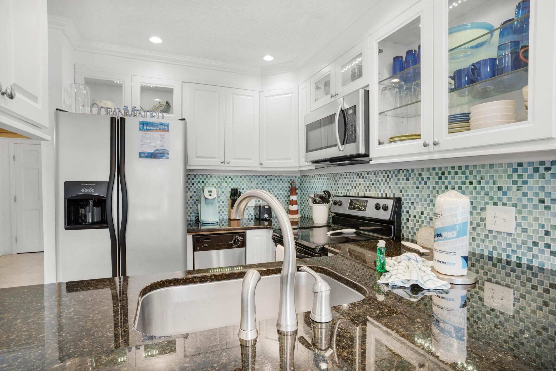 A modern kitchen with white cabinets, a stainless steel refrigerator, a microwave, and a sink with a faucet.