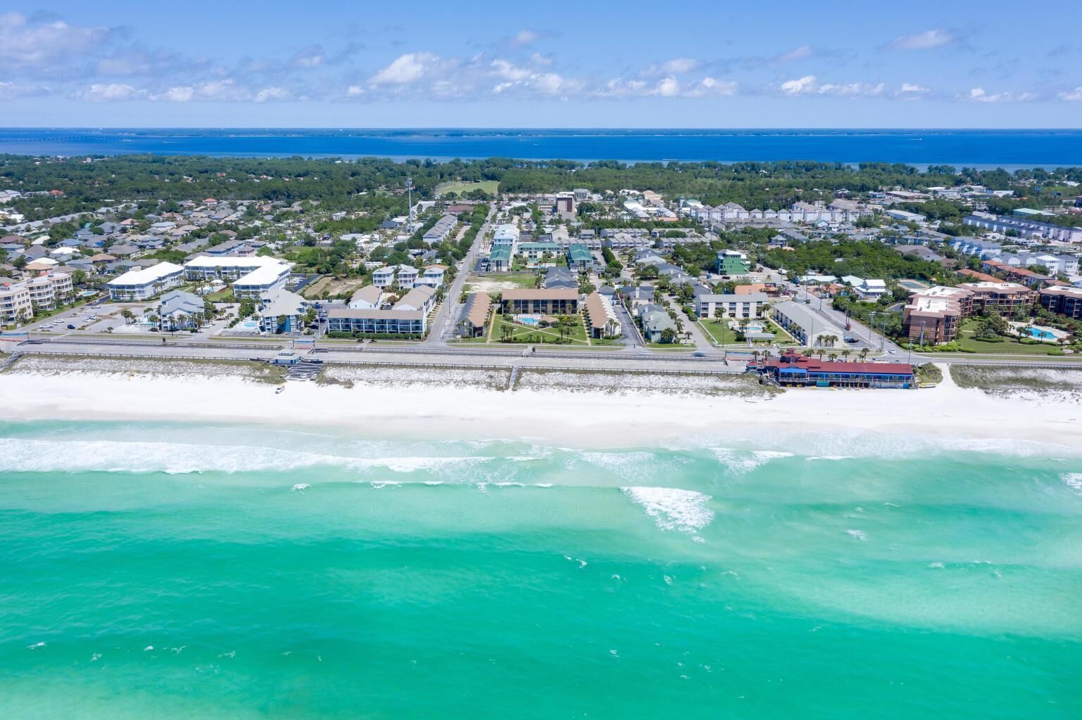 An aerial view of a coastal town with a beachfront, residential buildings, and a marina.