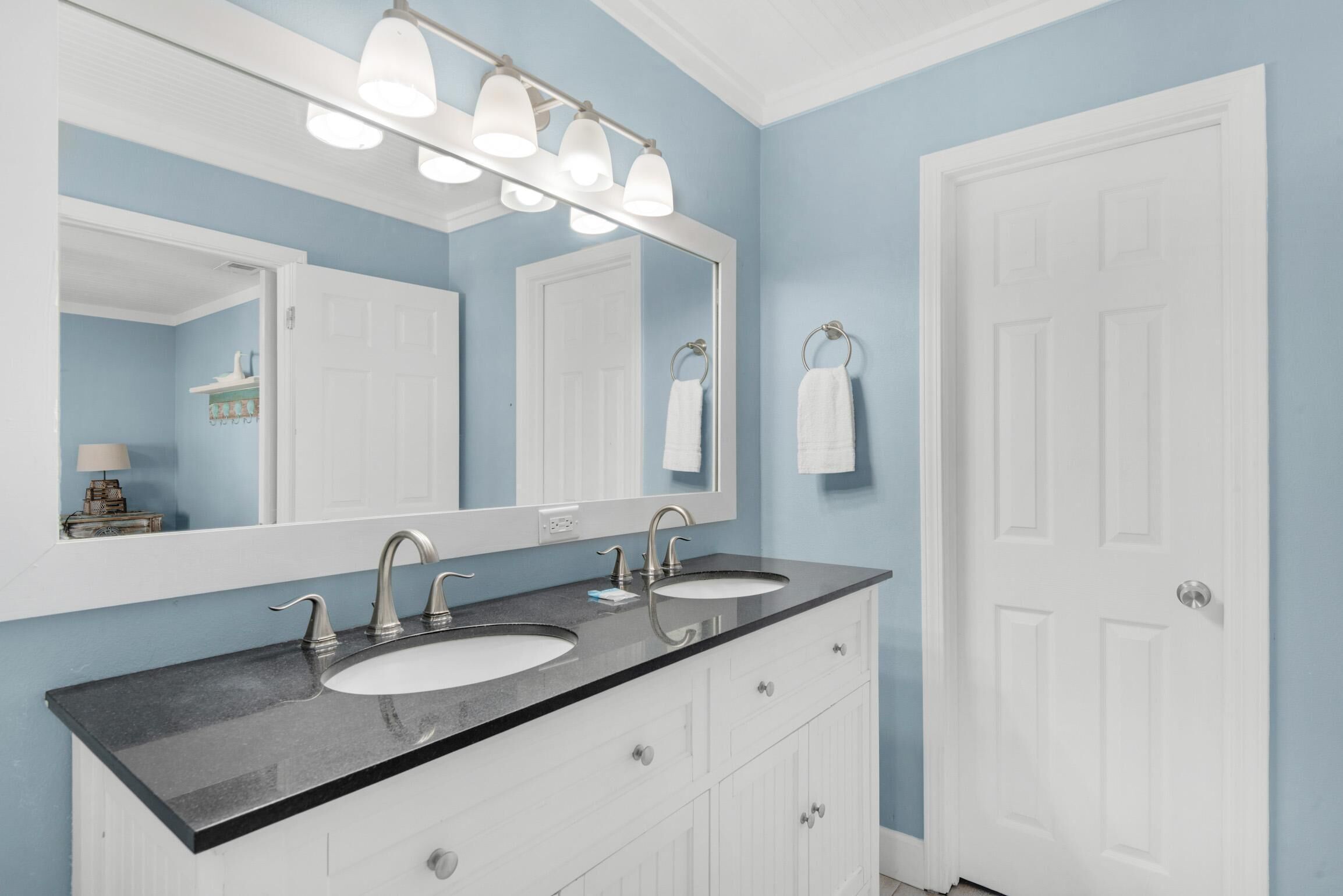 Une salle de bain avec deux lavabos, un grand miroir et une porte blanche.