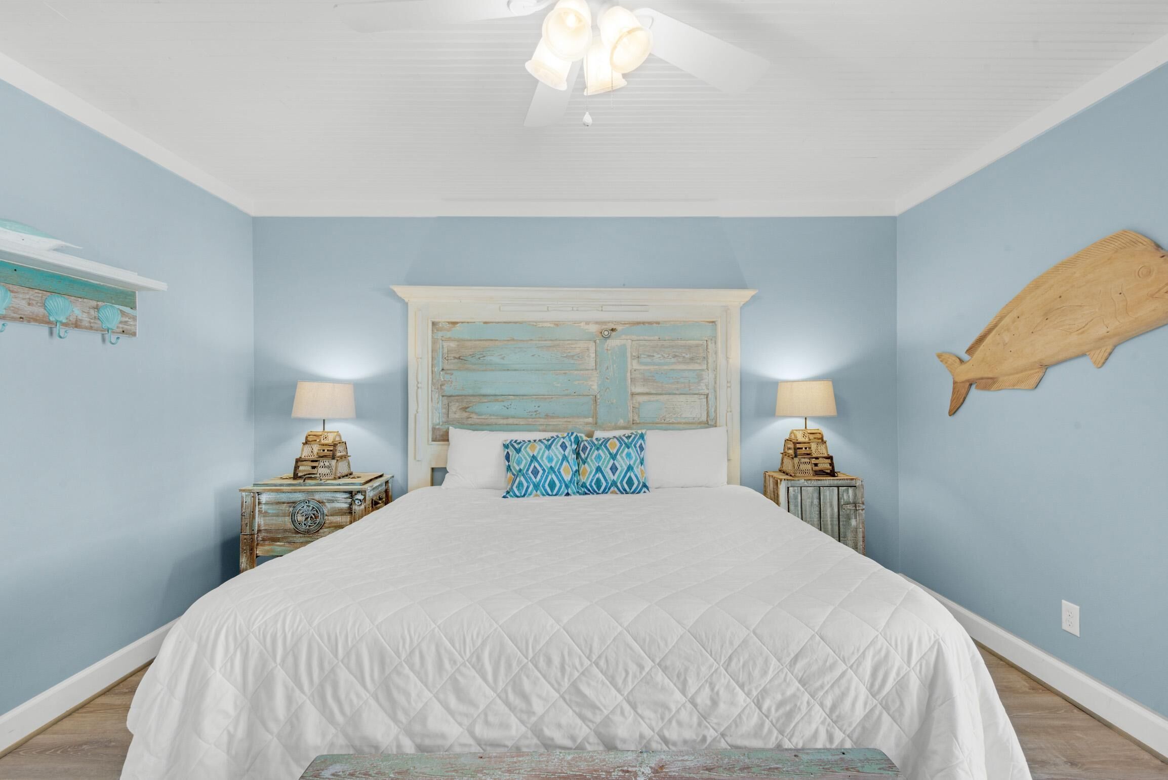 Una camera da letto con un letto grande, due comodini, una ventola a soffitto e un'ornamento a forma di pesce appeso al muro.