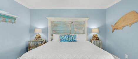 Una camera da letto con un letto grande, due comodini, una ventola a soffitto e un'ornamento a forma di pesce appeso al muro.