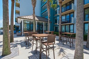 An outdoor patio area with tables and chairs, surrounded by palm trees and a building with multiple balconies. - Bayside at Sandestin 6770 (Miramar Beach)