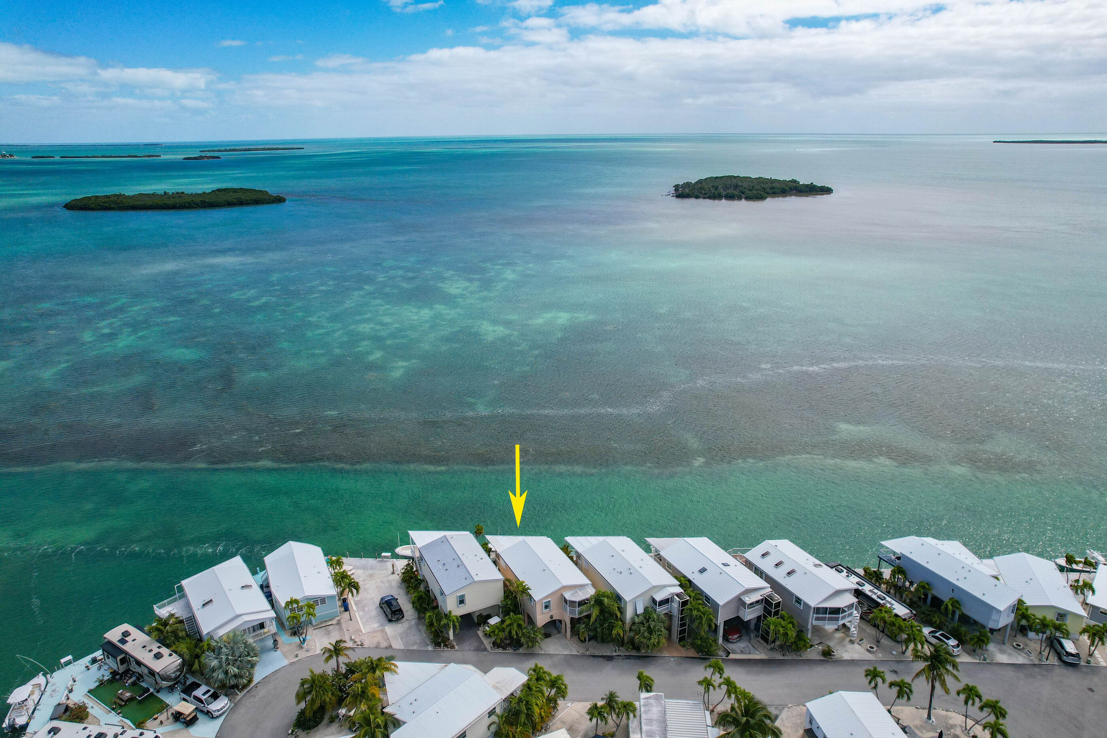 An aerial view of a coastal resort with multiple buildings, clear turquoise waters, and small islands in the distance.