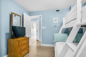 Un dormitorio con literas, un aparador de madera, un televisor y una puerta que da a otra habitación.